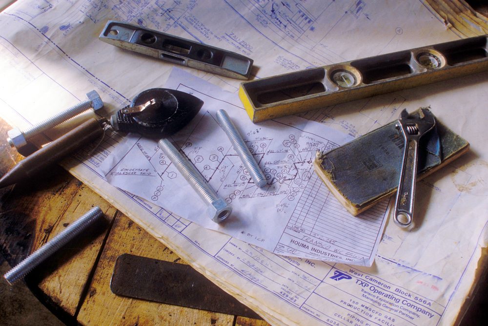 Piping drawings on a workbench with a level, wrench and bolts